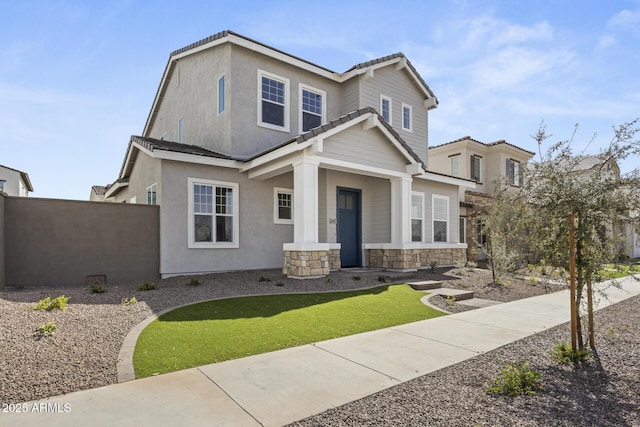 view of front of home featuring a tiled roof, fence, stone siding, and stucco siding