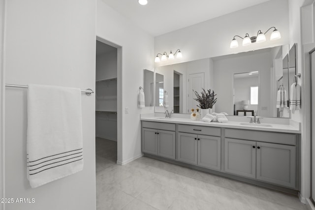 full bathroom featuring a sink, a walk in closet, baseboards, and double vanity