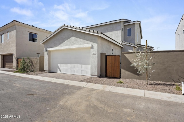 view of front of home with a gate, fence, stucco siding, a garage, and decorative driveway