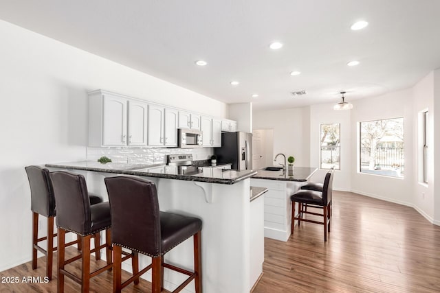 kitchen with a breakfast bar area, stainless steel appliances, wood finished floors, white cabinets, and tasteful backsplash