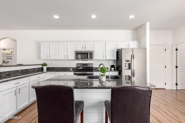 kitchen with appliances with stainless steel finishes, white cabinets, a sink, and a kitchen bar