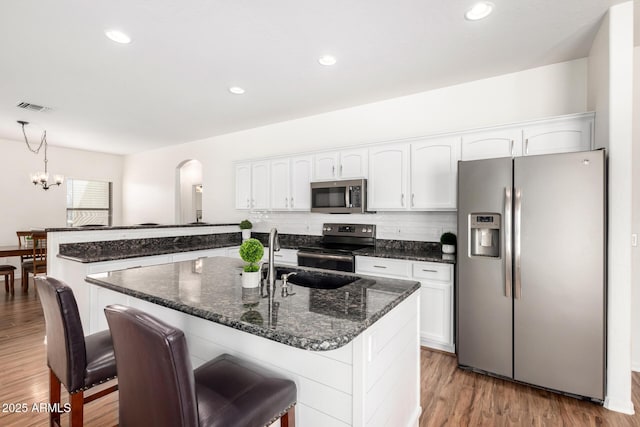 kitchen featuring appliances with stainless steel finishes, white cabinetry, a sink, wood finished floors, and a peninsula