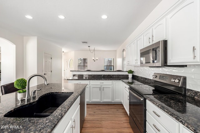 kitchen with stainless steel appliances, white cabinets, a sink, wood finished floors, and a peninsula