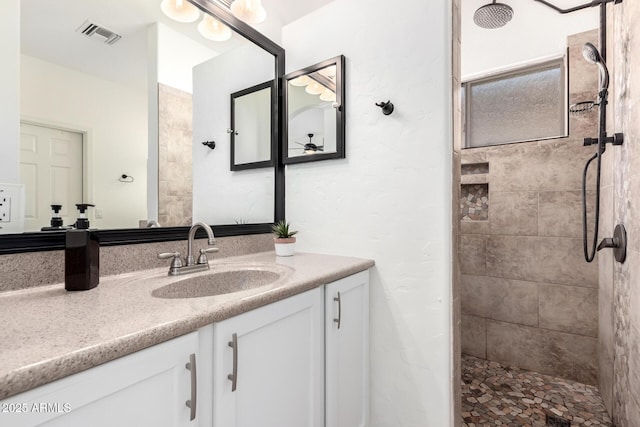 bathroom featuring visible vents, a tile shower, and vanity