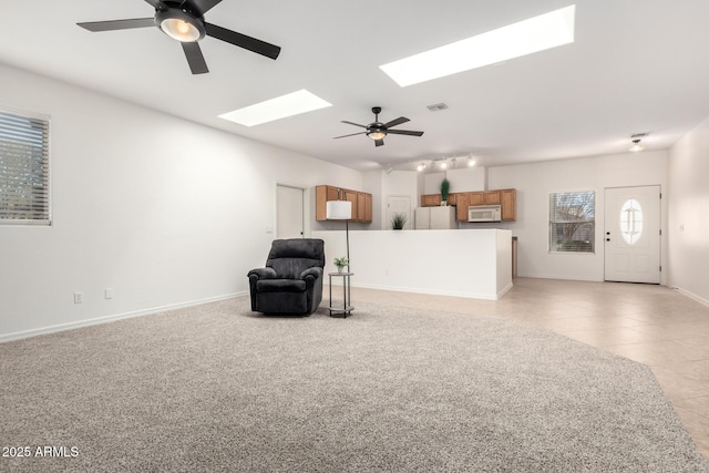 interior space featuring a skylight, light tile patterned floors, visible vents, baseboards, and ceiling fan