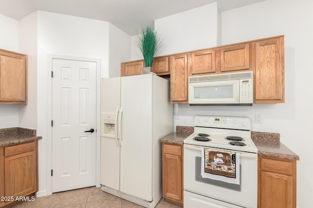 kitchen with dark stone countertops, white appliances, and light tile patterned flooring