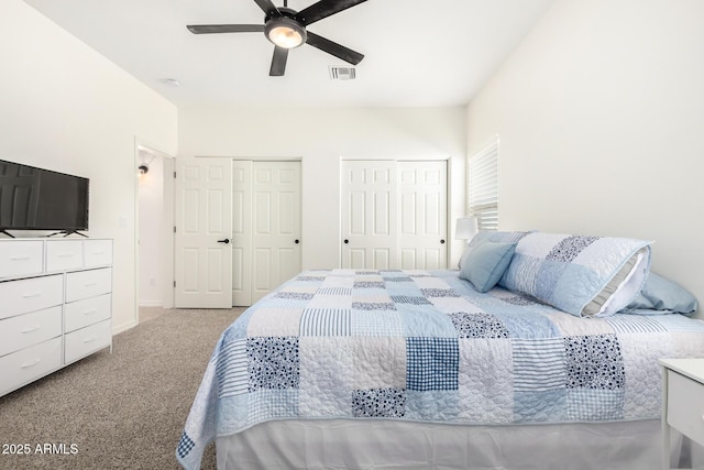 carpeted bedroom featuring a ceiling fan, visible vents, and two closets