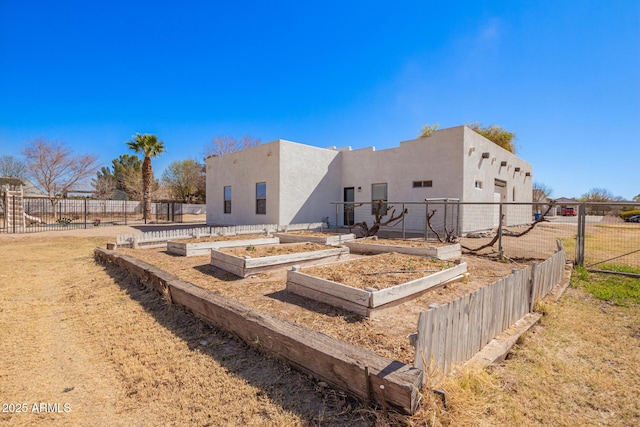 rear view of house featuring fence, a garden, and stucco siding