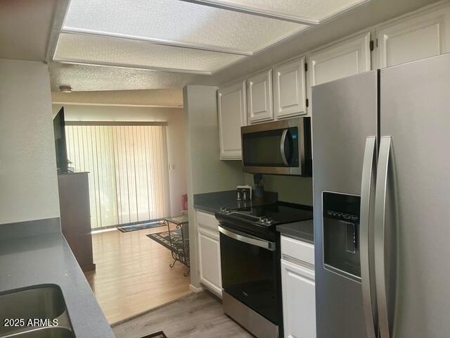 kitchen featuring dark countertops, white cabinets, light wood-style floors, and appliances with stainless steel finishes