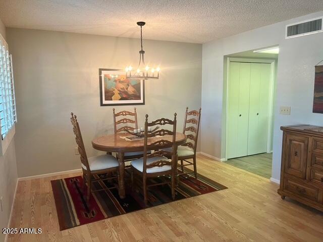 dining area with a chandelier, visible vents, a textured ceiling, and wood finished floors