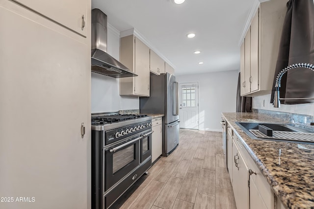 kitchen with sink, crown molding, wall chimney exhaust hood, dark stone countertops, and appliances with stainless steel finishes