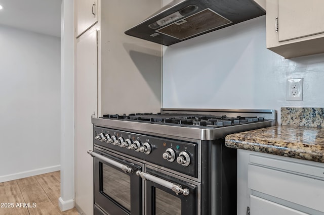 kitchen featuring dark stone counters, ventilation hood, high end stainless steel range, light hardwood / wood-style floors, and white cabinetry