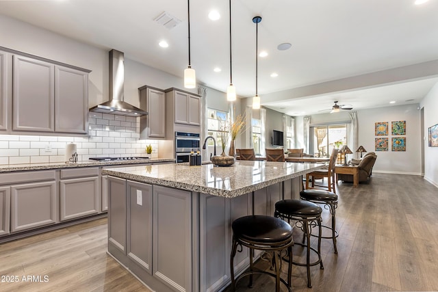 kitchen with gray cabinetry, stainless steel appliances, visible vents, wall chimney exhaust hood, and tasteful backsplash