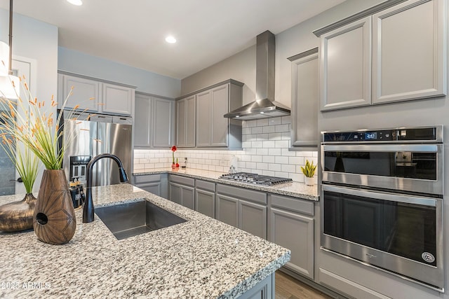 kitchen with stainless steel appliances, wall chimney range hood, a sink, and gray cabinetry