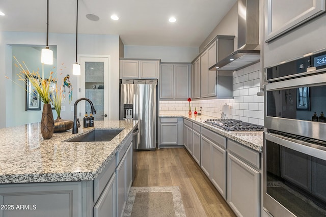 kitchen with a sink, stainless steel appliances, wall chimney range hood, and gray cabinets