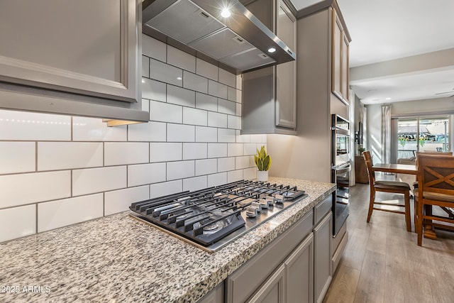 kitchen featuring light wood-style flooring, appliances with stainless steel finishes, gray cabinets, and exhaust hood