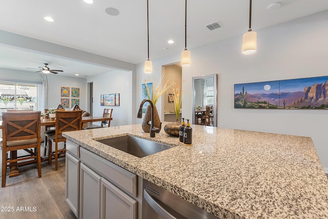 kitchen with hanging light fixtures, light wood finished floors, visible vents, and a sink