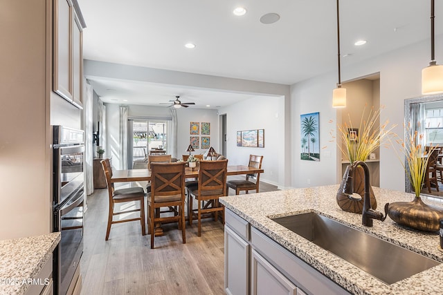 kitchen featuring light stone counters, recessed lighting, a sink, light wood-style floors, and decorative light fixtures