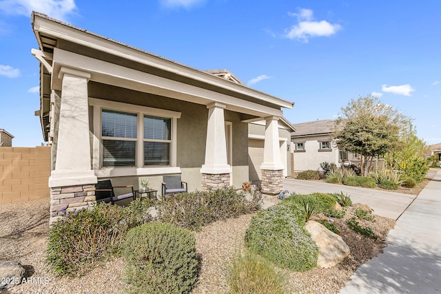 view of front of house with covered porch, concrete driveway, stone siding, and stucco siding