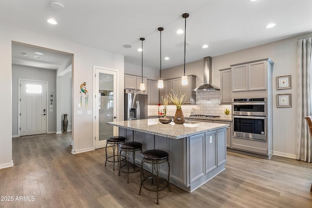 kitchen with appliances with stainless steel finishes, gray cabinets, wall chimney exhaust hood, and wood finished floors