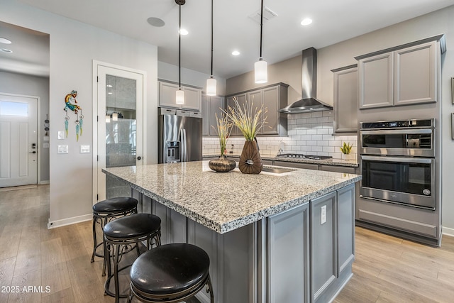 kitchen featuring stainless steel appliances, gray cabinets, light wood-style floors, and wall chimney range hood