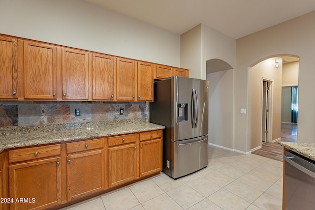 kitchen with backsplash, light stone counters, light tile patterned flooring, and stainless steel appliances