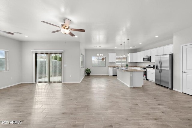 kitchen with appliances with stainless steel finishes, an island with sink, decorative light fixtures, ceiling fan with notable chandelier, and white cabinetry