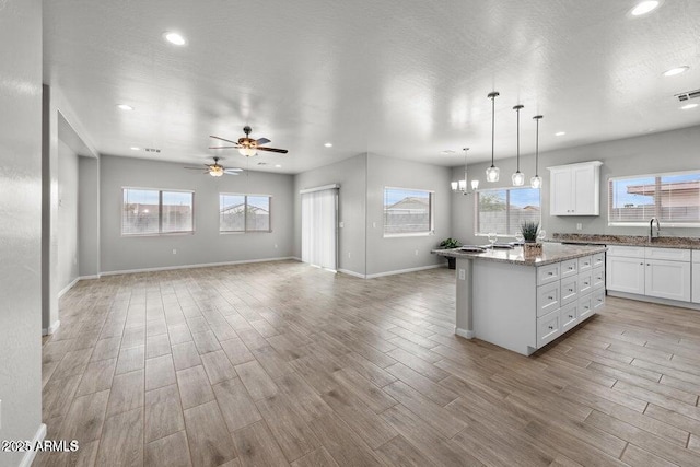 kitchen with light wood-type flooring, white cabinets, pendant lighting, a center island, and sink