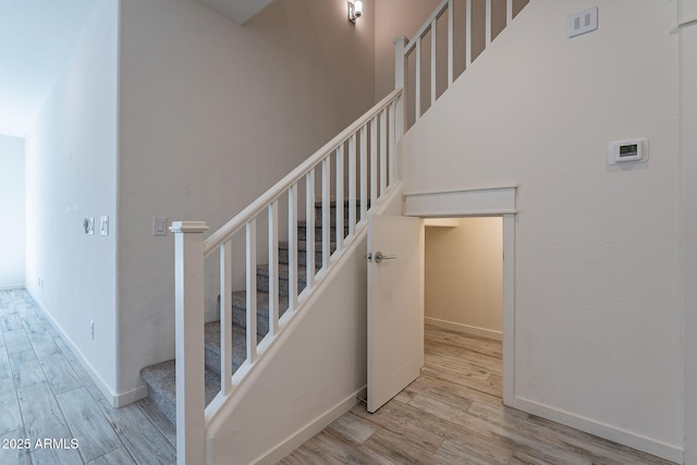 staircase with a towering ceiling, visible vents, baseboards, and wood finished floors