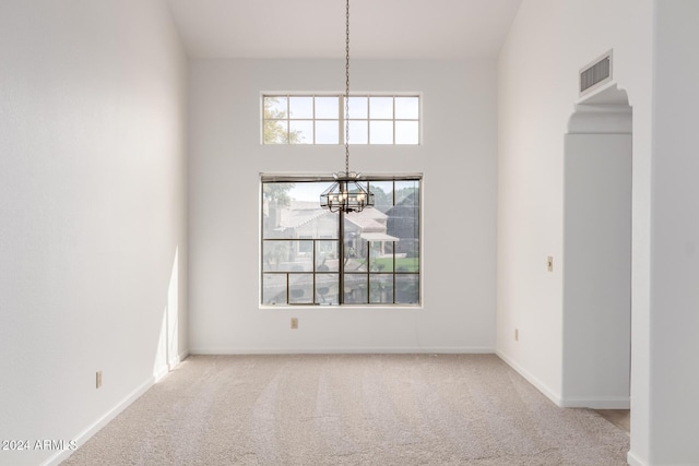 unfurnished dining area with light carpet, a towering ceiling, and a notable chandelier