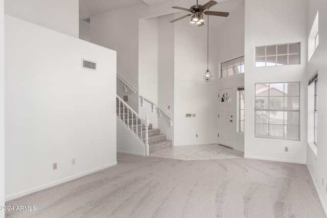 foyer entrance featuring ceiling fan, a towering ceiling, and light carpet