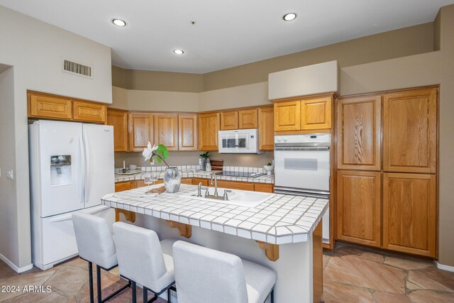 kitchen with an island with sink, a notable chandelier, hanging light fixtures, white appliances, and tile countertops