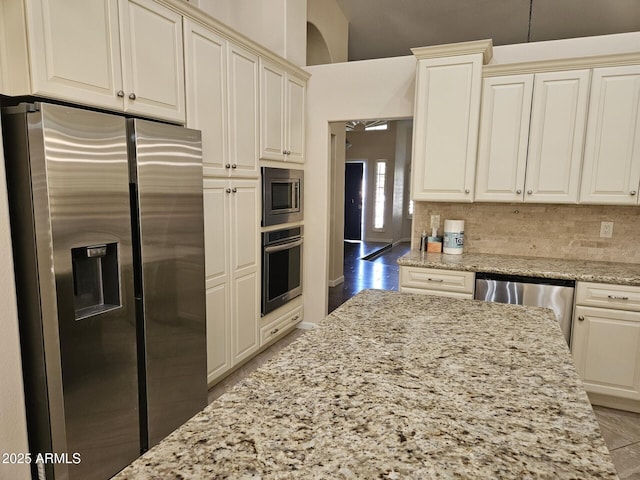 kitchen featuring light stone counters, backsplash, appliances with stainless steel finishes, and light wood-type flooring