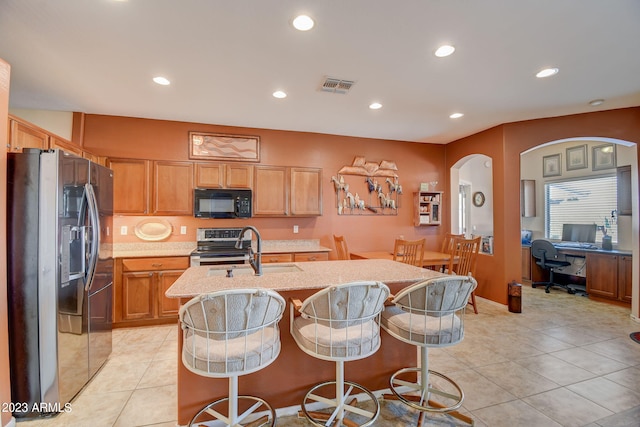 kitchen with sink, stainless steel appliances, a kitchen bar, a center island with sink, and light tile patterned flooring