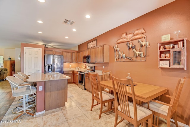 kitchen featuring a breakfast bar, a center island with sink, light stone countertops, light tile patterned floors, and stainless steel appliances