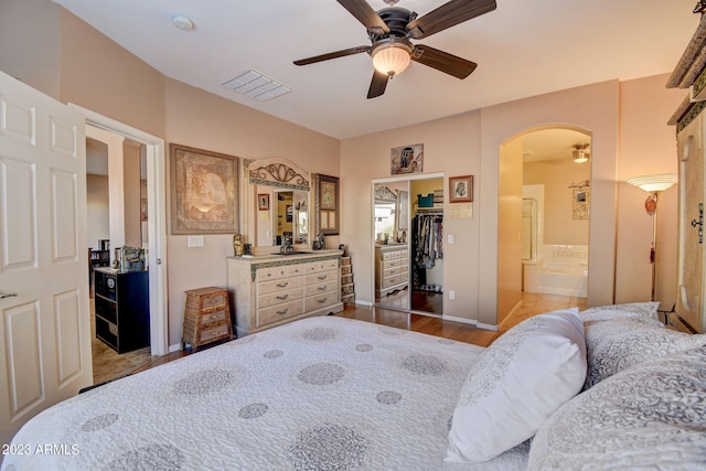 bedroom featuring light wood-type flooring, ceiling fan, a spacious closet, connected bathroom, and a closet