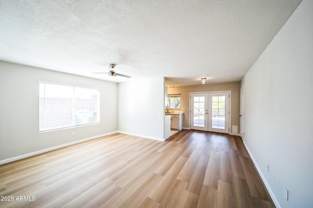 unfurnished living room featuring a textured ceiling, french doors, light wood-type flooring, and baseboards