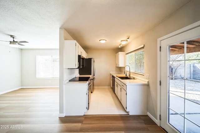 kitchen with stainless steel appliances, a sink, light countertops, white cabinets, and light wood-type flooring