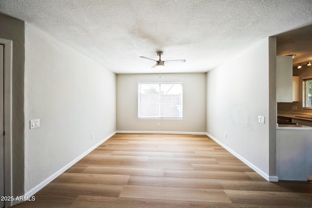 spare room featuring light wood-style floors, baseboards, and a textured ceiling