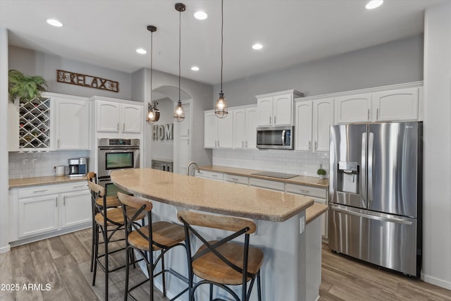 kitchen with white cabinets, appliances with stainless steel finishes, a center island, decorative light fixtures, and a breakfast bar