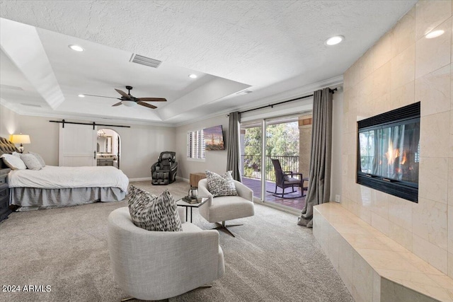 carpeted bedroom with a tray ceiling, a fireplace, access to outside, a barn door, and ceiling fan