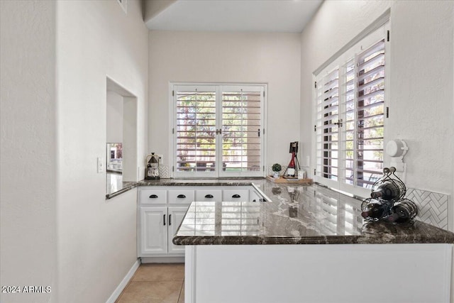 kitchen featuring dark stone counters, kitchen peninsula, white cabinetry, and light tile patterned flooring