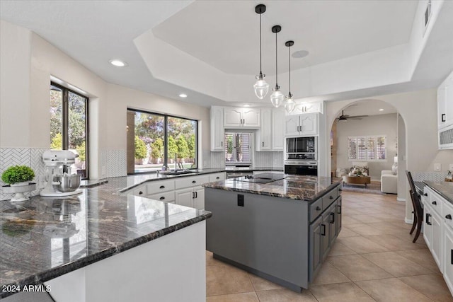 kitchen featuring dark stone countertops, a raised ceiling, hanging light fixtures, and white cabinetry