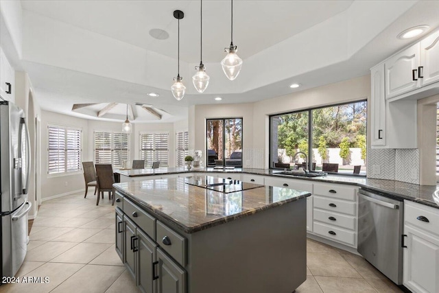 kitchen featuring white cabinetry, stainless steel appliances, a tray ceiling, a center island, and dark stone counters