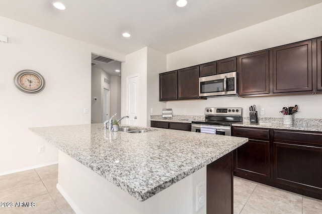 kitchen with light tile patterned flooring, an island with sink, light stone countertops, appliances with stainless steel finishes, and sink