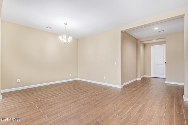 empty room featuring a notable chandelier and light hardwood / wood-style floors