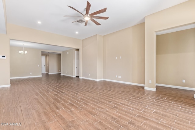 empty room featuring ceiling fan with notable chandelier and light wood-type flooring