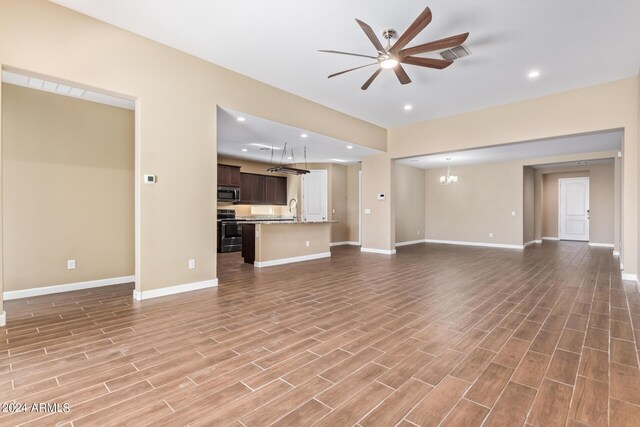 unfurnished living room with ceiling fan with notable chandelier, sink, and light hardwood / wood-style flooring