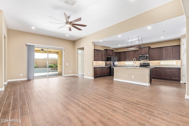 kitchen with an island with sink, light hardwood / wood-style floors, ceiling fan, and appliances with stainless steel finishes