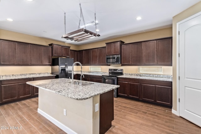 kitchen featuring light stone counters, an island with sink, sink, light hardwood / wood-style flooring, and appliances with stainless steel finishes